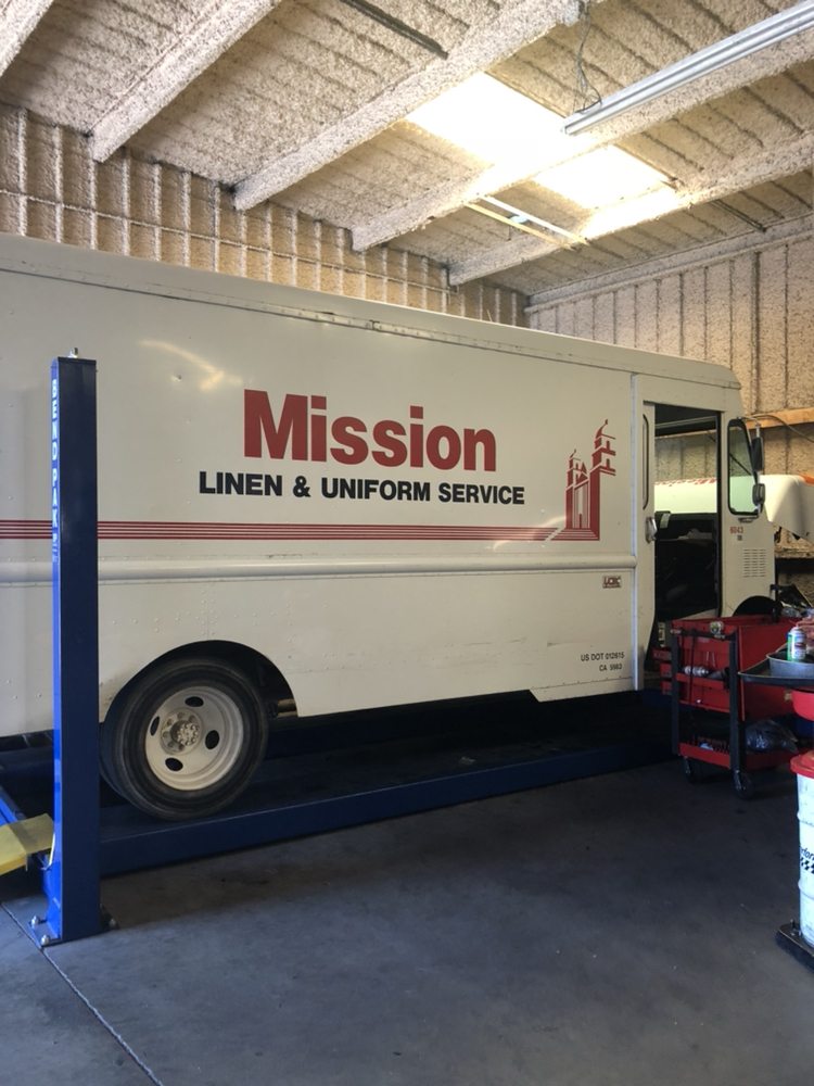 A white box truck raised on a lift inside the shop